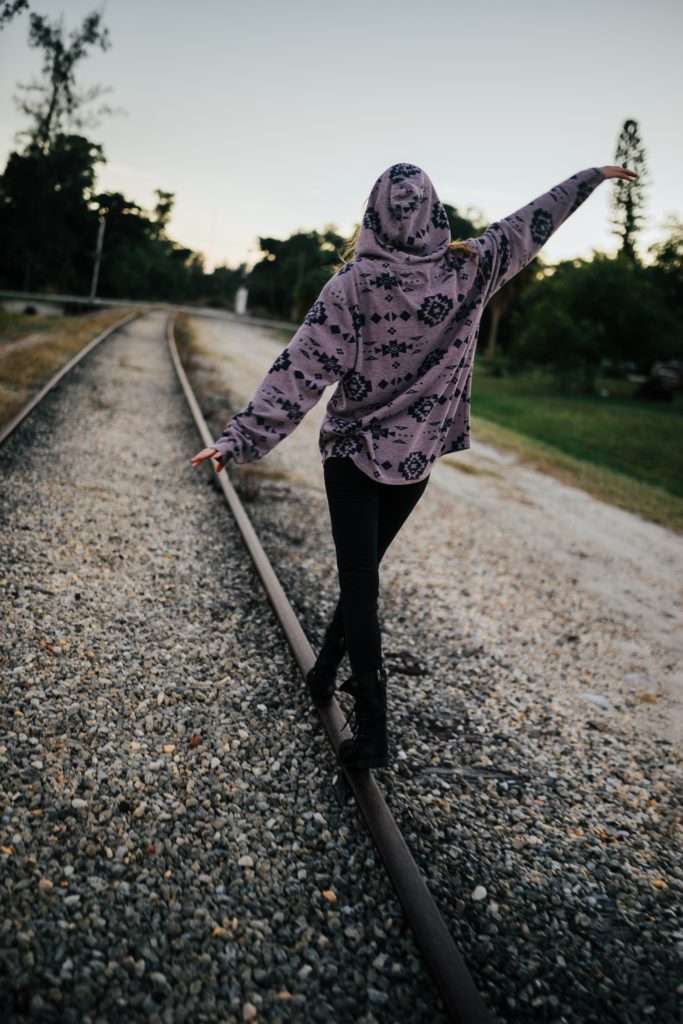 Teenager balancing on a railroad track with arms extended. 