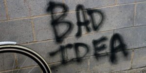 Spray painted of "bad idea" on a wall next to a bicycle wheel.