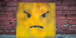 An angry emoticon in front of a brick wall.